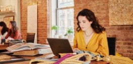 Image of woman wearing yellow working on laptop at a table