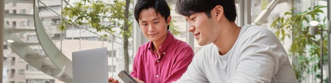 Two businessmen siting and discussing over a mobile phone and a laptop.