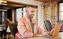An individual working at a desk in a shared space with their laptop.